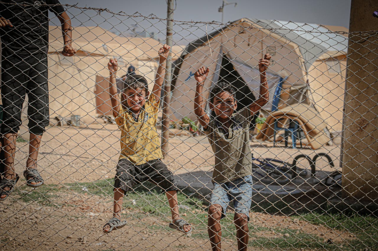 home-hero Children laugh and play on a fence in a Syrian refugee camp, capturing a moment of joy.